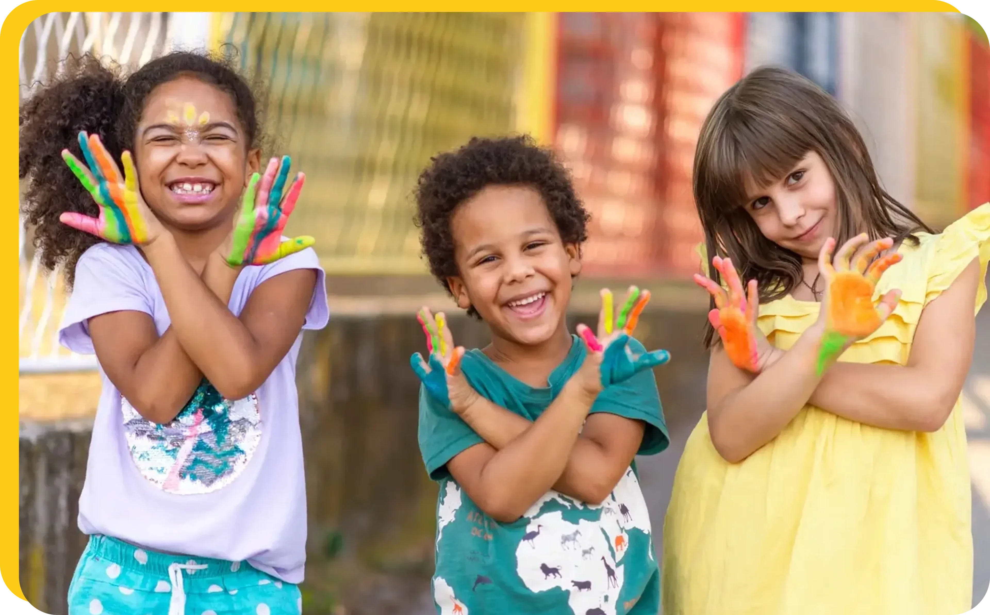 Three children with painted hands smiling and posing outdoors.
