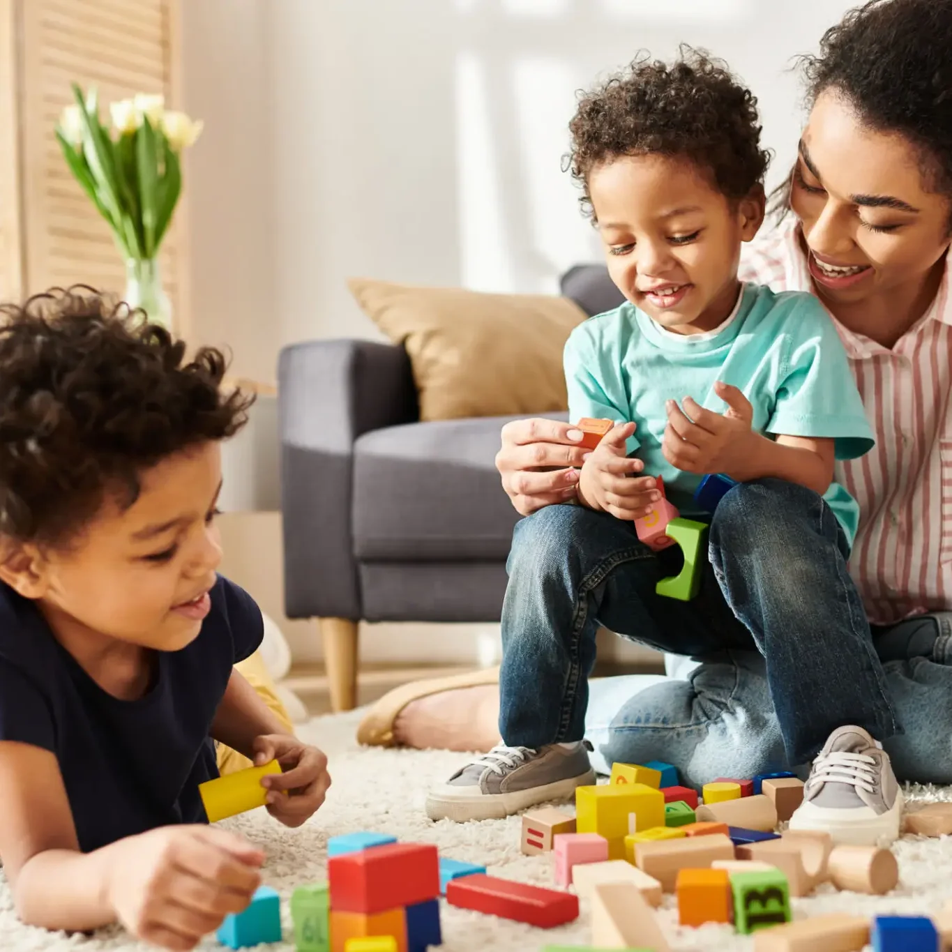 A mother and two children playing with colorful building blocks indoors.